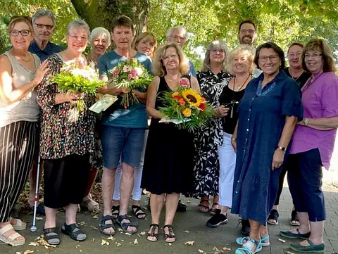 Eine Gruppe von Ehrenamtlichen vor einem Baum. Drei Menschen haben Blumensträuße in den Händen.